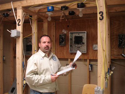 Photo 3. Judges. After the students completed the practical installation portion of testing, volunteer judges reviewed and scored each student’s work. Scott Jolliff reviews the Gold Medalist’s work.