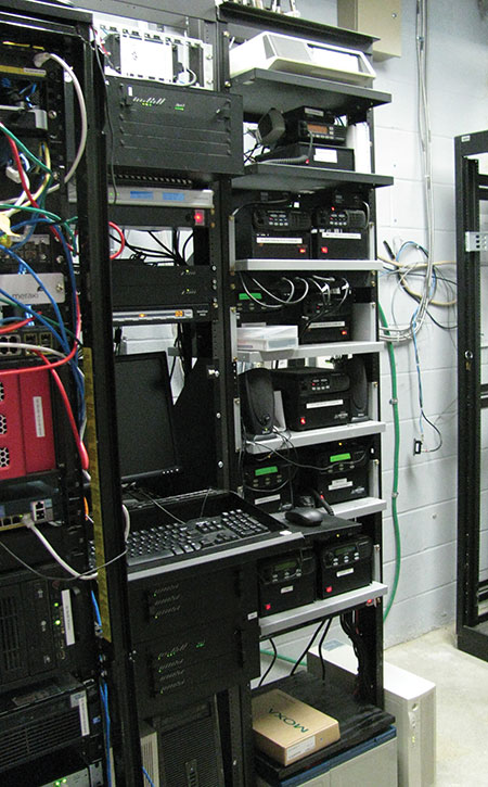 Figure 4. Equipment on adjacent IT server racks (at left) and radio racks (at right) suffered major damage from the 2013 lightning strike. It is believed that the racks shared a CAT-5 Ethernet cable to a time-synching computer. When lightning energy entered the building due to grossly inadequate (and incorrect) grounding and lightning protection, the shared CAT-5 cable provided a path for that energy to damage both the IT and communication systems.