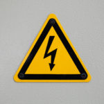 High voltage triangle warning sign mounted on gray metal wall