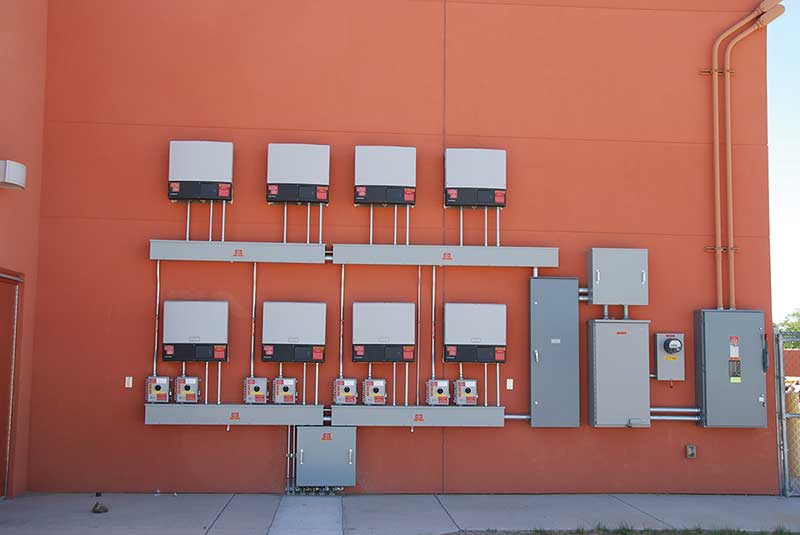 Photo 6. Eight PV systems with eight dc disconnects below eight utility-interactive inverters feeding an ac combining panel (right of center) and then to a single ac system disconnect on the far right. Courtesy of John Wiles