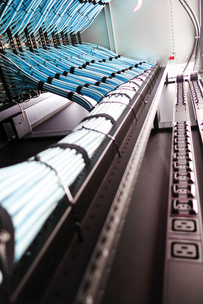 Photo 1. Structured cabling entering rack-mounted PDUs. Modern data centers rely on carefully coordinated A/B power paths, proper separation of power and communications conductors, and verification of conductor ampacity in high-fill environments.